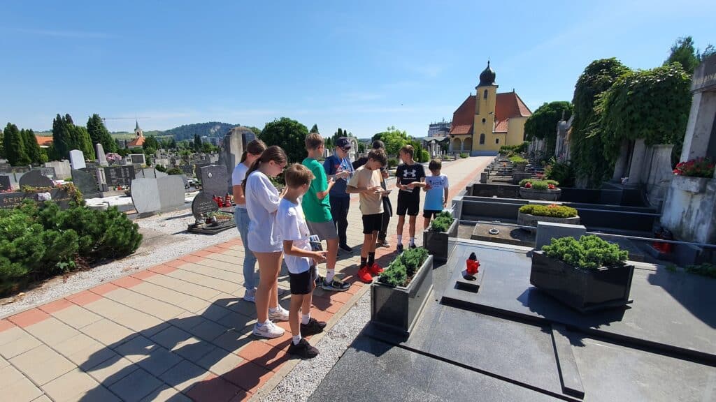 School kids exploring Pobrežje cemetery in Maribor with mobile devices