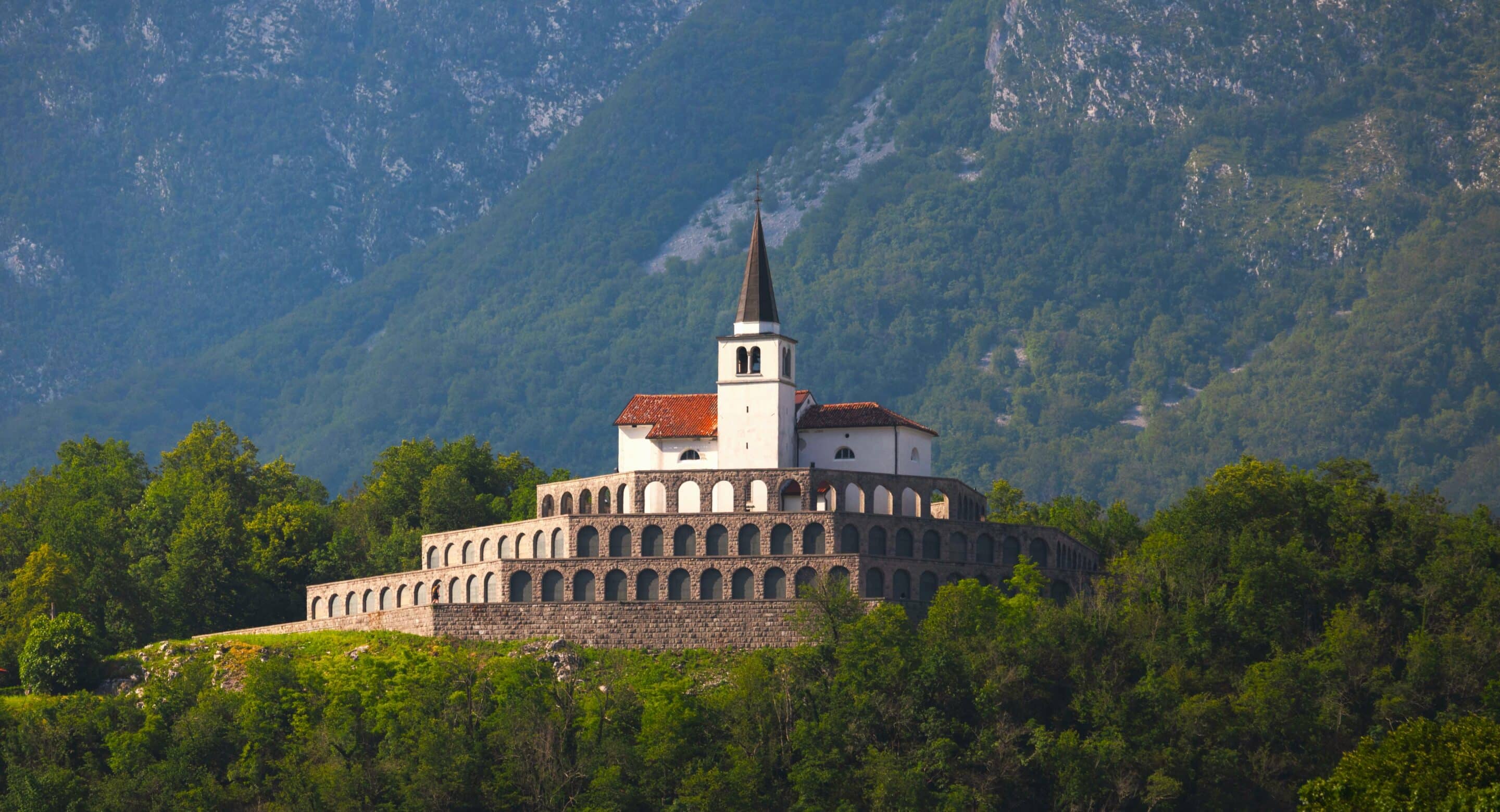 Church above terraced stone arches surrounded by forested Slovenian hills