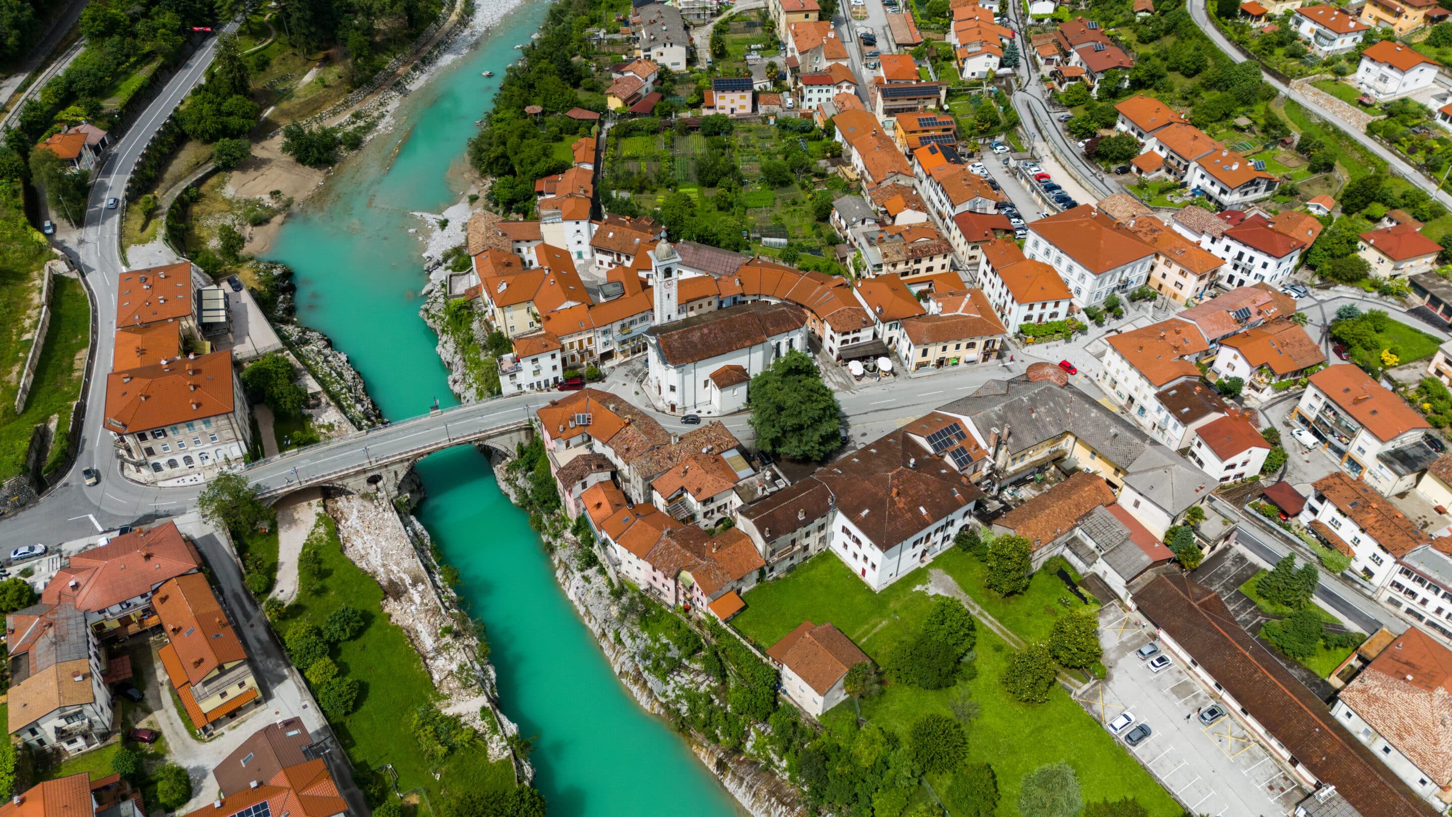 Aerial view of Kanal ob Soci with the turquoise Soca river, a stone bridge and a church tower